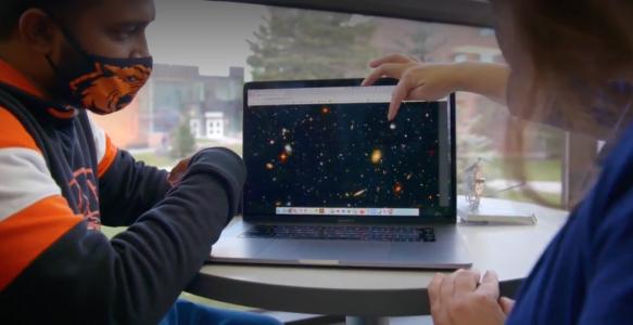 Two researchers on our team point at an image of galaxies on a laptop screen